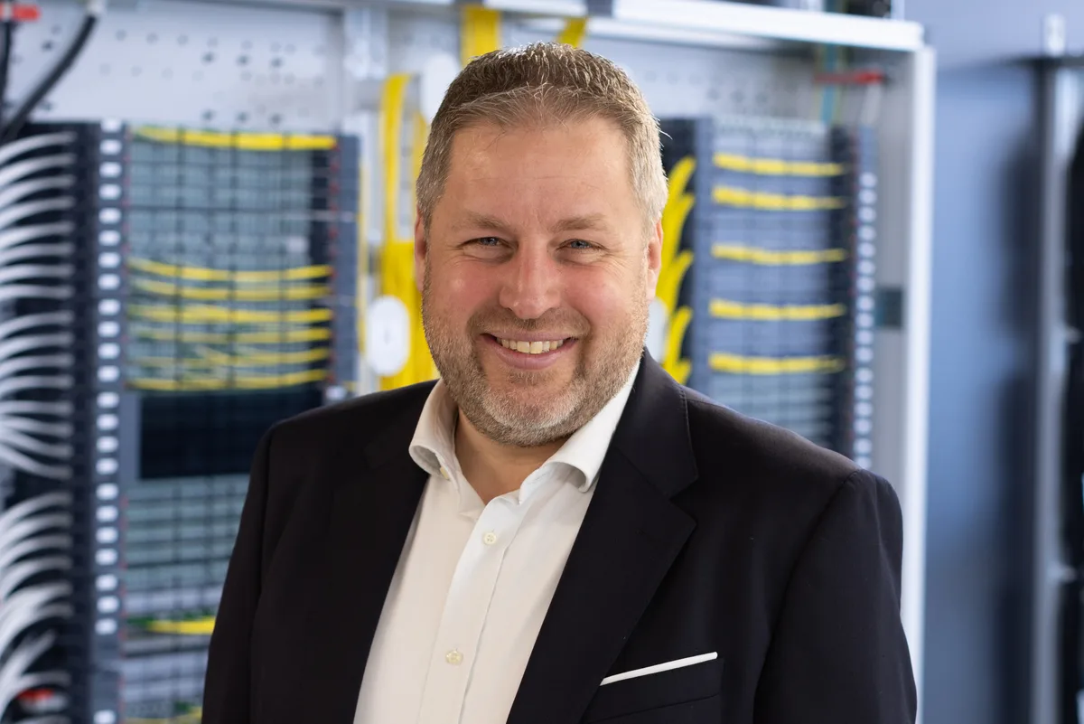 Hannes Grubinger ist als Chief Product & Marketing Officer (CPMO) für das globale Produktportfolio, die strategischen Marktsegmente und das Marketing von R&M verantwortlich. Porträt von Hannes Grubinger. Er steht vor einem Rack mit gelben Kabeln.